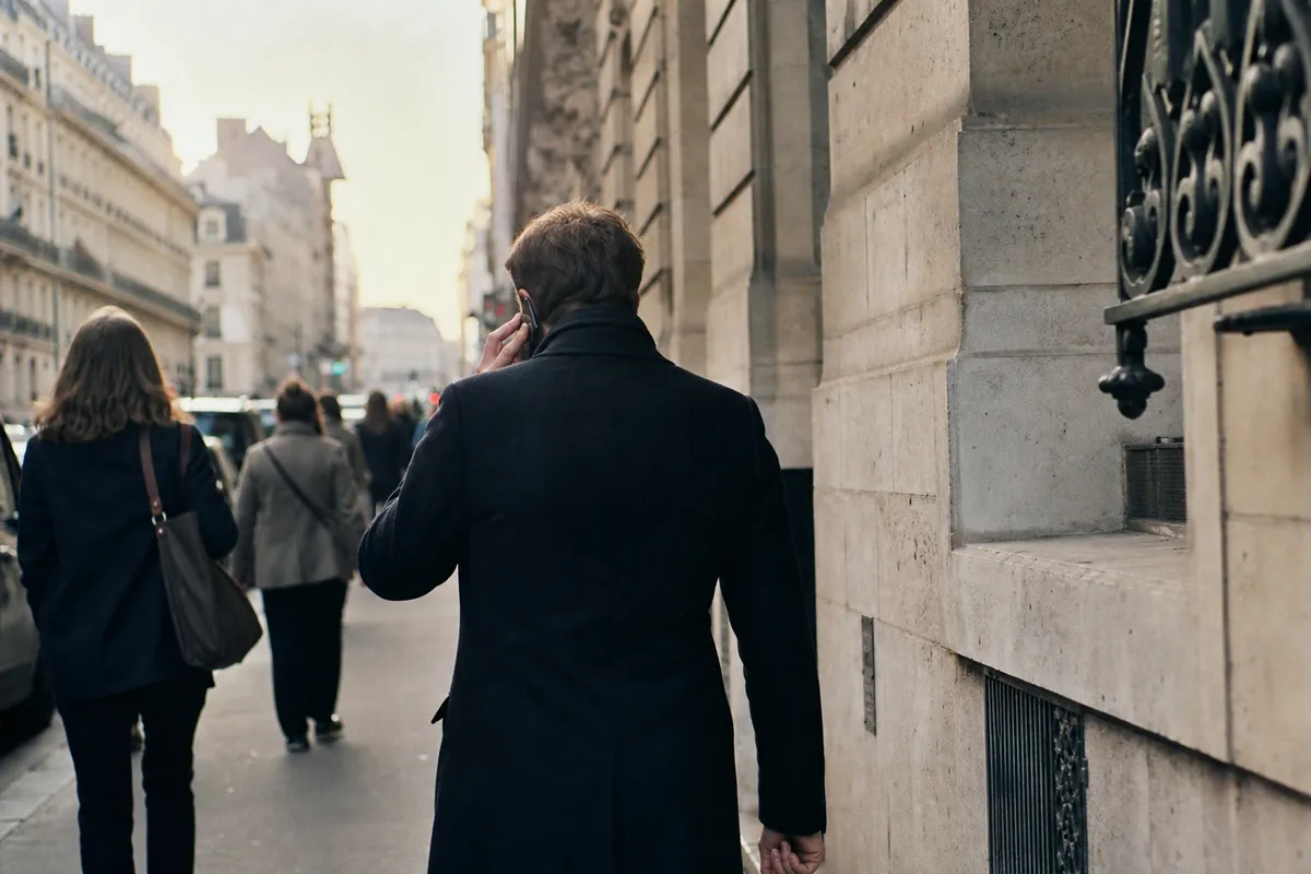 Passant au téléphone dans une rue haussmannienne, cherchant à joindre son syndic